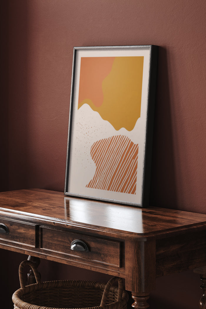 Modern abstract art poster with yellow and orange shapes framed on a console table against a maroon wall