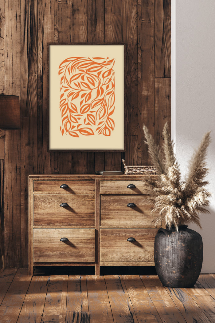 Abstract orange leaf pattern artwork in a frame on a rustic wooden wall above a wooden cabinet with decorative dried pampas grass