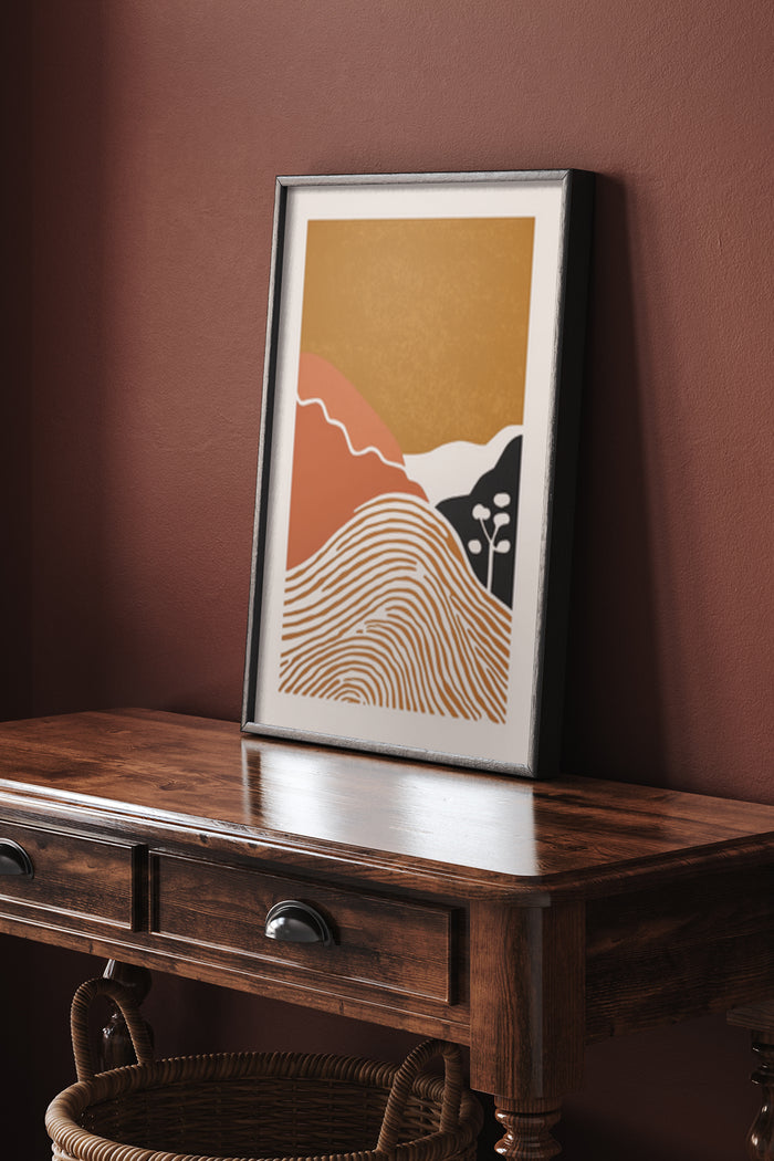 Framed abstract mountain landscape poster with warm color palette displayed on wooden console table