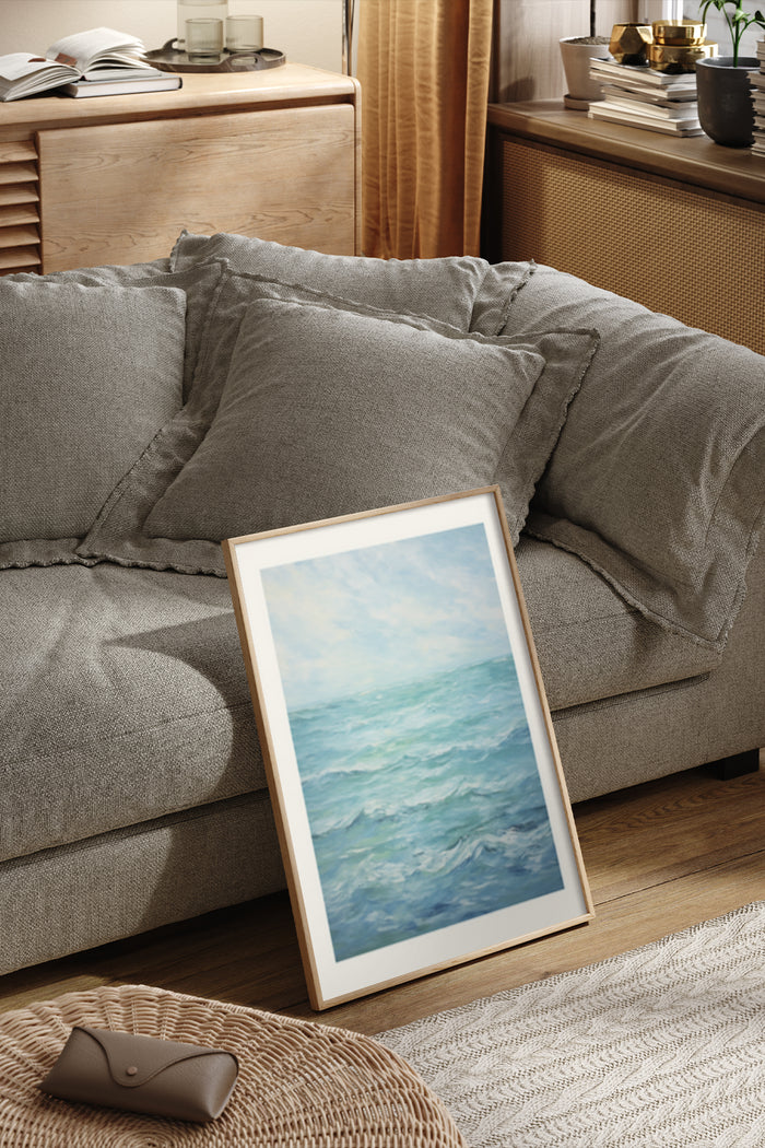Abstract coastal ocean painting in white frame leaning against grey sofa in a modern home setting