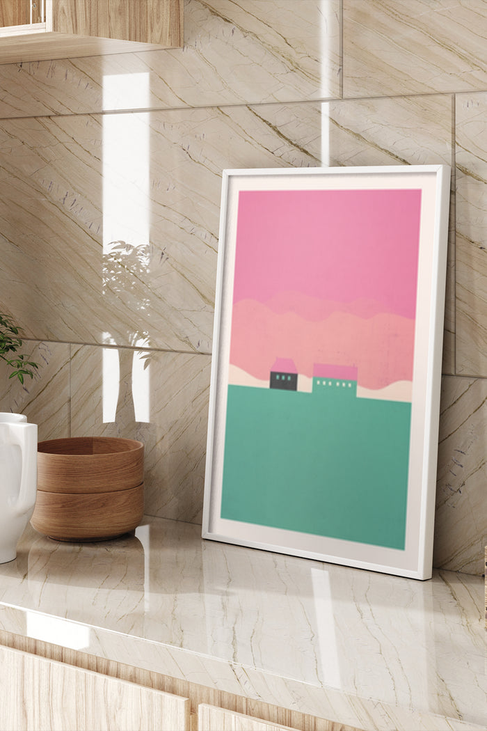 Minimalist artwork of a pink sky and green hills with silhouetted houses, framed poster on marble wall