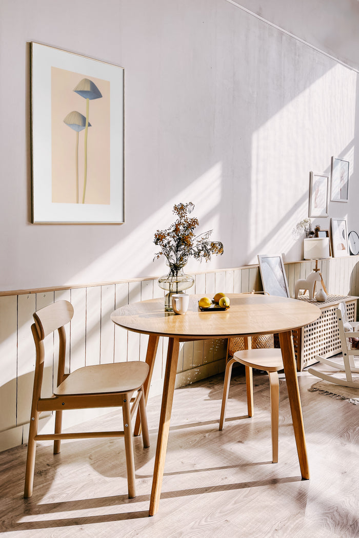 Stylish interior with modern art poster of geometric blue flowers above a wooden Scandinavian style dining table in a brightly sunlit room