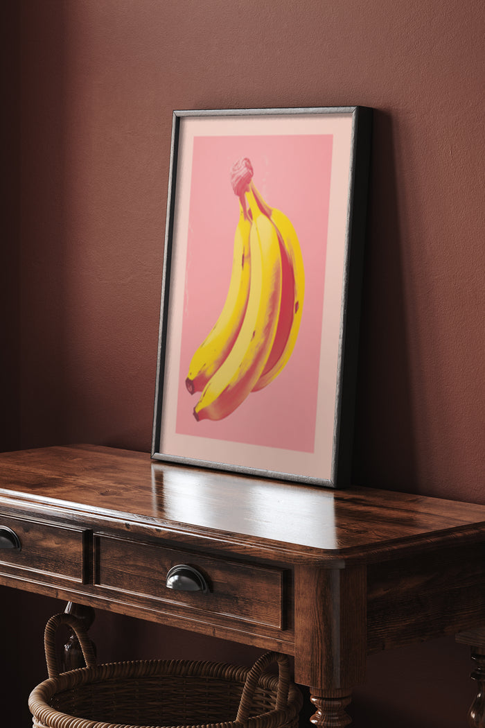 A contemporary framed poster of yellow bananas on a pink background displayed on a wooden console in a stylish interior setting