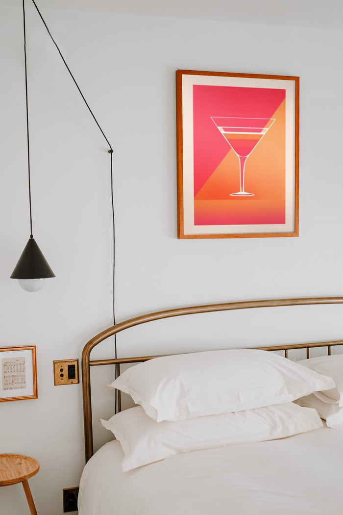 Modern cocktail glass poster in warm tones hanging above bed in a chic bedroom interior