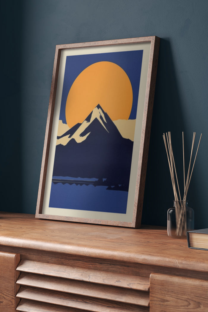 Modern minimalist framed poster of a stylized mountain sunrise set against a blue background displayed in a cozy interior