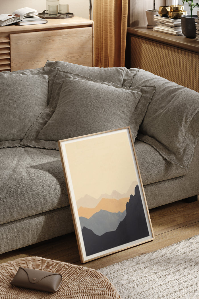 Modern abstract mountain landscape poster leaning against a sofa in a cozy living room setting