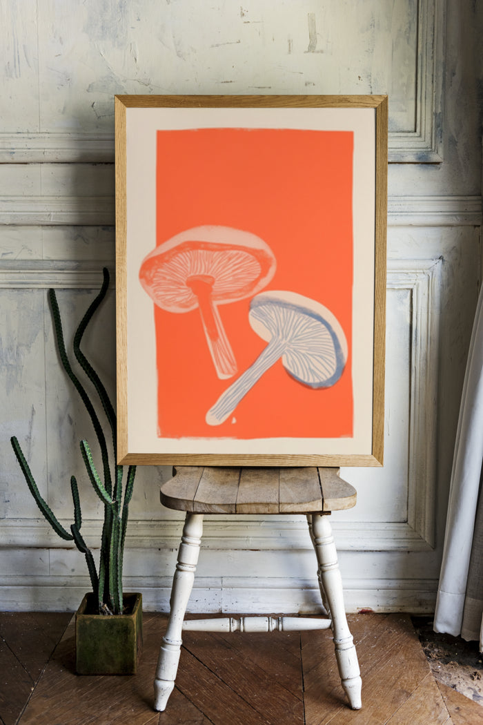 Modern mushroom artwork poster displayed on wooden easel in a vintage styled interior with potted cactus
