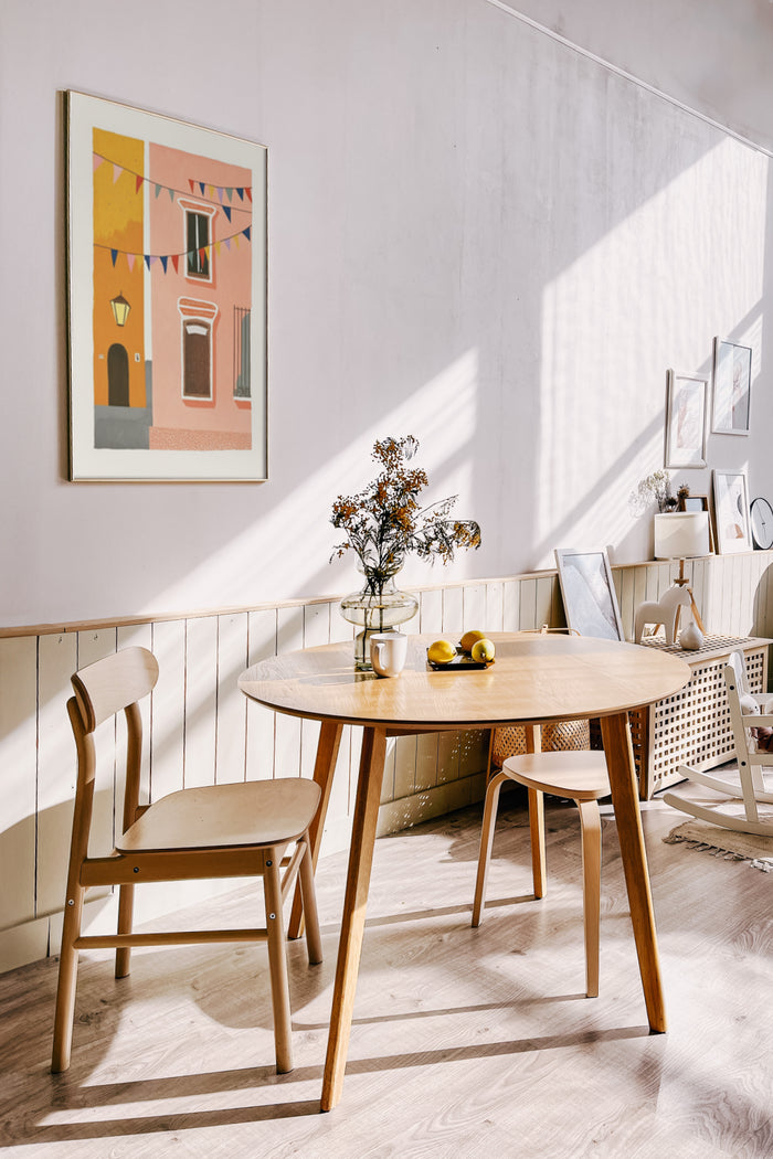 Contemporary wall poster in a sunlit dining room with wooden round table and Scandinavian chairs