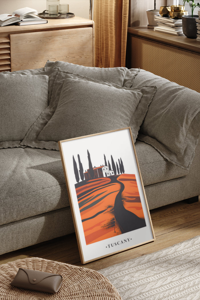 Tuscany landscape poster featuring a house and cypress trees with orange hues framed and displayed on the floor leaning against a couch in a cozy living room interior
