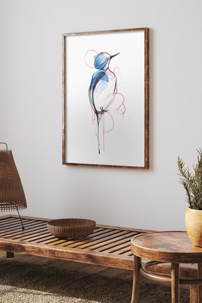 Abstract blue and red bird illustration in a wooden frame, on a white wall above a bench and side table with wicker lamp and plant decor