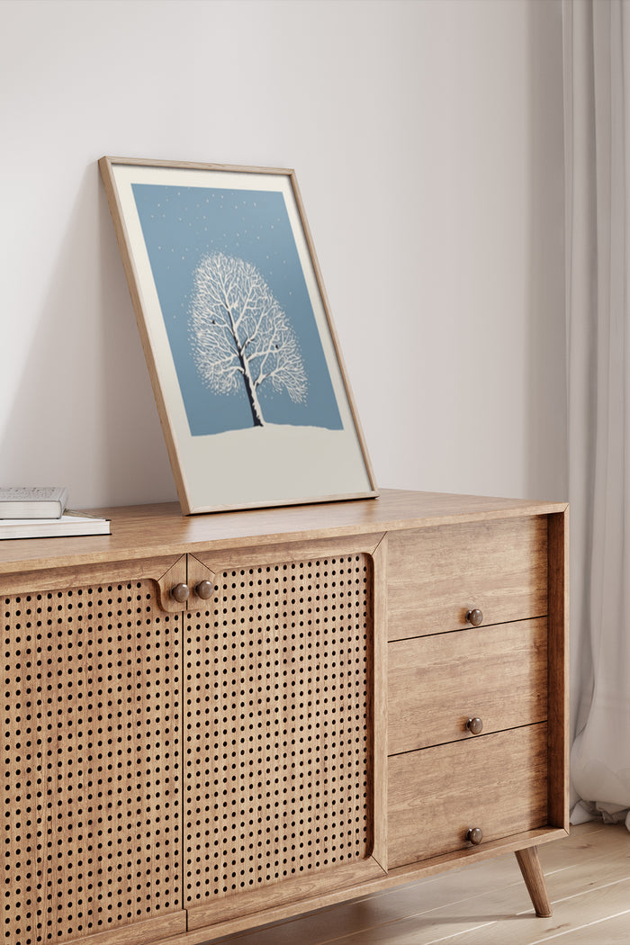 Minimalist winter tree artwork poster displayed in a wooden frame on a sideboard