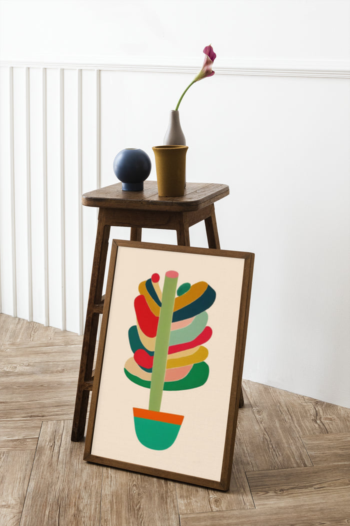 Colorful abstract art poster displayed in a wooden frame on the floor leaning against a wall with a decorative side table and vase