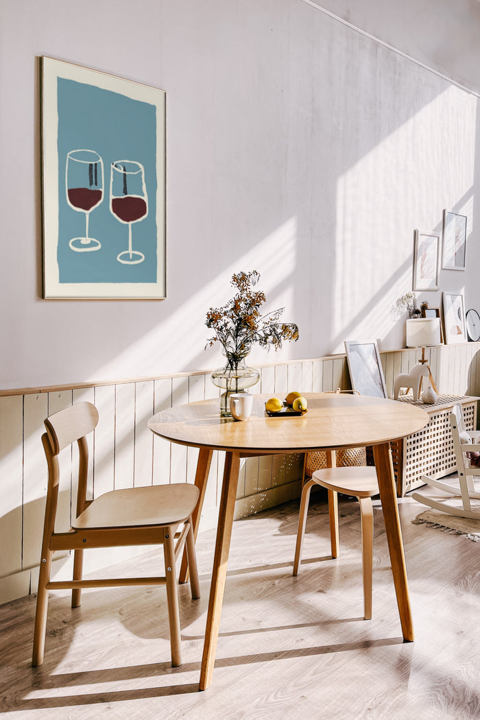 Contemporary dining room with sunlight featuring a framed poster of two wine glasses