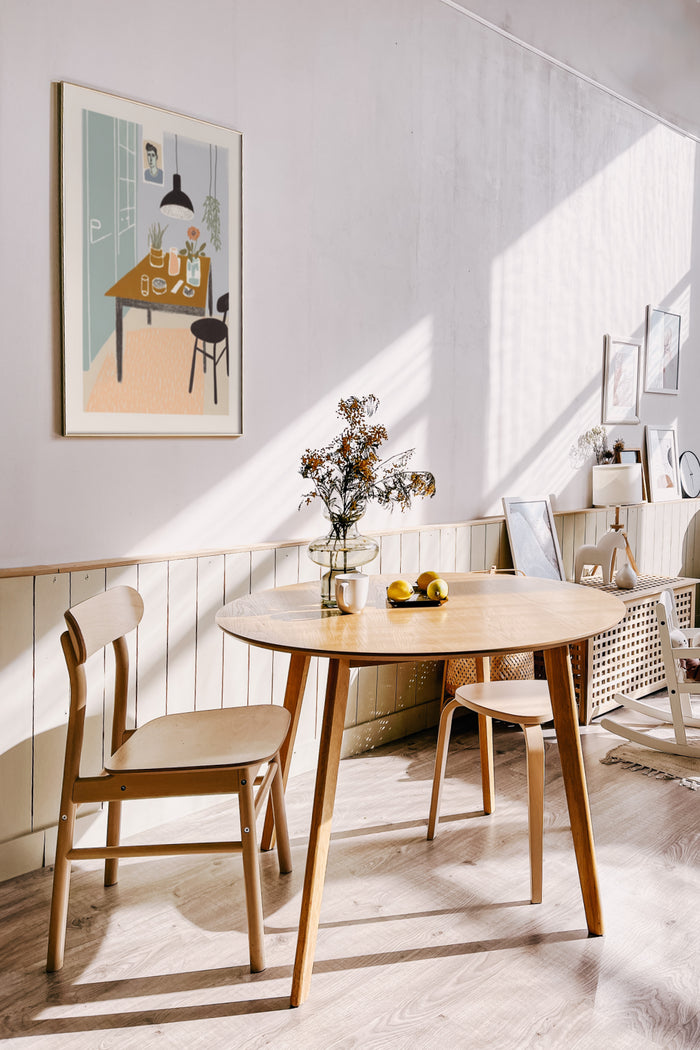 Contemporary dining room interior with sunlight featuring a modern art poster, wooden table, and Scandinavian-style chairs