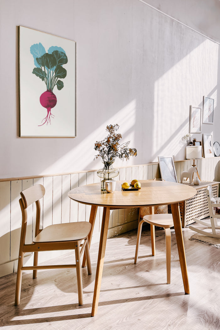 Stylish dining room interior with sunlight, wooden table and chairs, and a framed poster of a beet on the wall