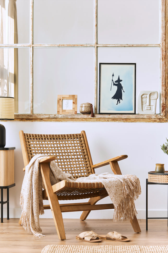 Modern interior design featuring a witch silhouette art poster, woven chair with throw blanket, and stylish home decor