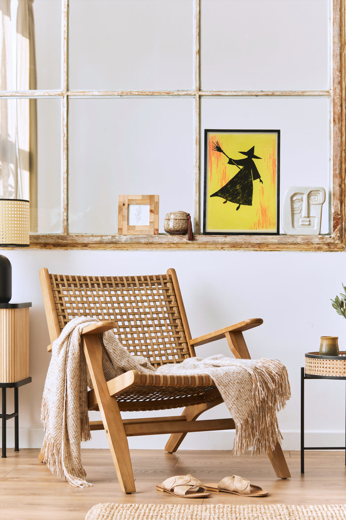 Contemporary witch silhouette art poster on wall in a trendy interior design with wooden chair and cozy throw