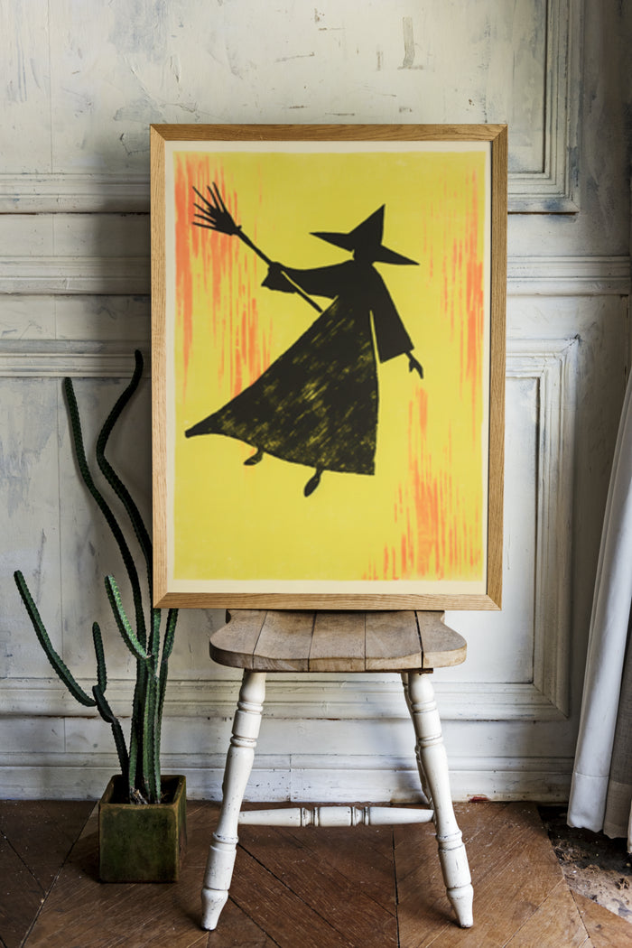 Modern witch silhouette artwork poster with vibrant yellow background displayed on wooden easel